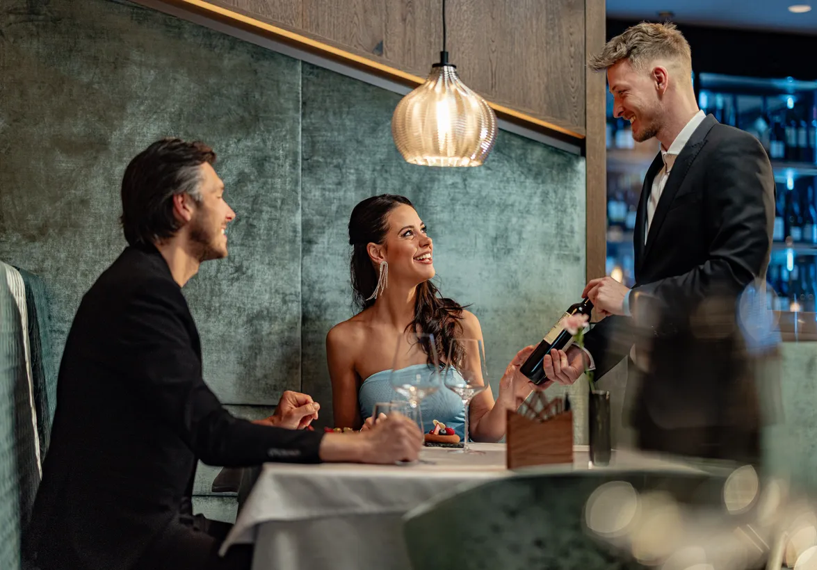 Sommelier präsentiert einem elegant gekleideten Paar eine Flasche Wein im Restaurant des Hotel Kronblick in Kiens