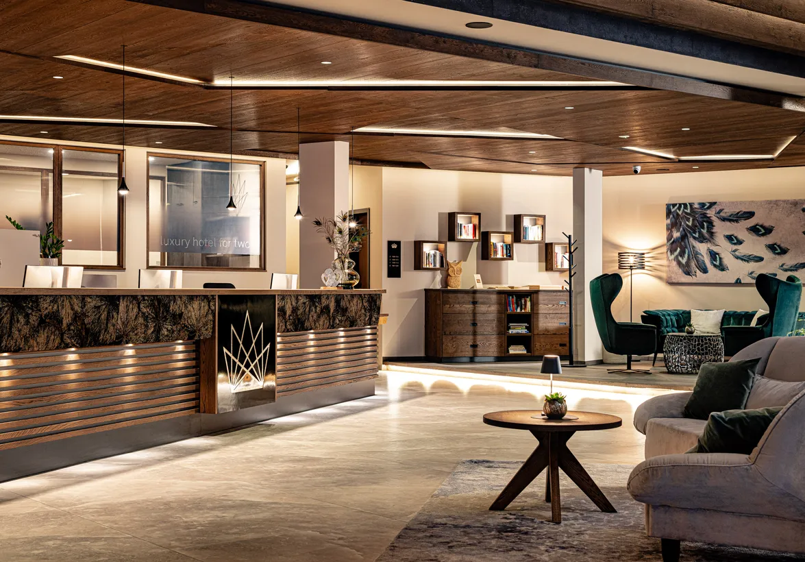 Lobby mit Rezeption, Holzdecke und gemütlicher Leseecke im Hotel Kronblick – Luxury Hotel for Two in Kiens
