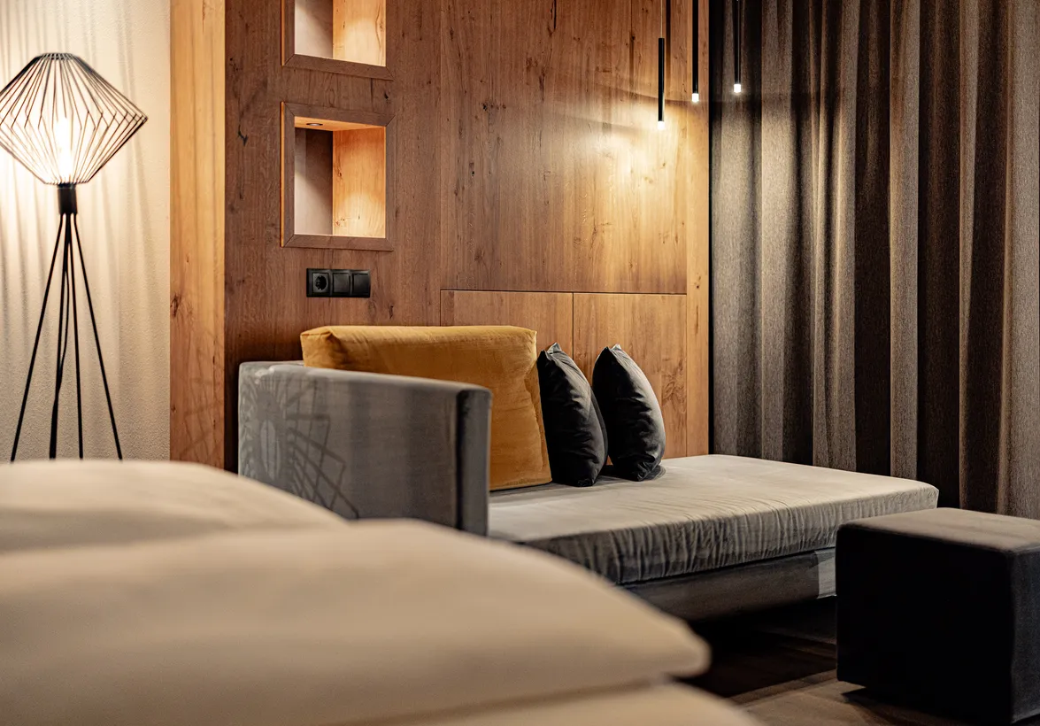 Gemütlicher Schlafbereich mit Sofa, Kissen und warmer Holzvertäfelung in einer Suite des Hotels Kronblick