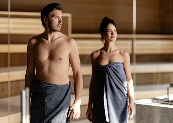 Paar in Handtüchern verlässt die Holzsauna im Wellnessbereich des Hotel Kronblick im Pustertal