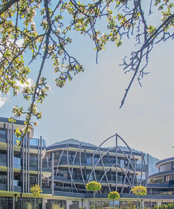 Moderne Fassade des Hotels Kronblick Leitgam mit geschwungener Stahlkonstruktion, gerahmt von blühenden Apfelbaumzweigen in Kiens