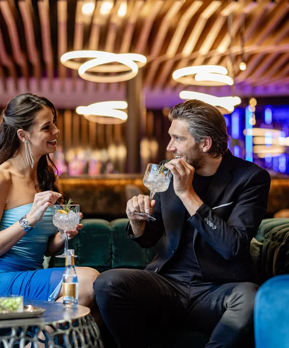 Paar trinkt Gin-Tonic-Cocktails auf Samtsofas in der stilvollen Bar-Lounge des Hotel Kronblick in Südtirol
