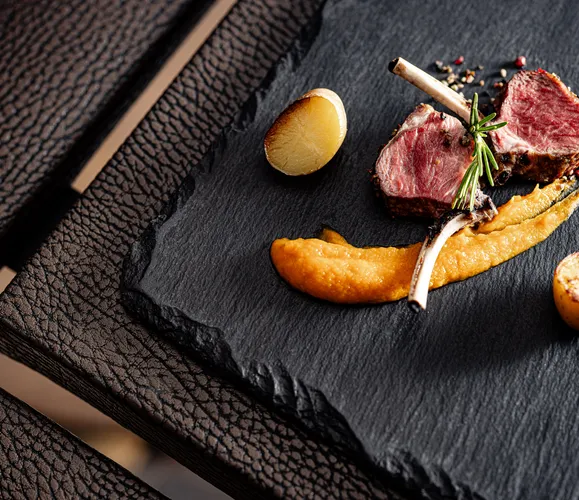 Rosa gebratene Lammkoteletts mit Süßkartoffelpüree und Rosmarin auf Schieferplatte im Hotel Kronblick Kiens