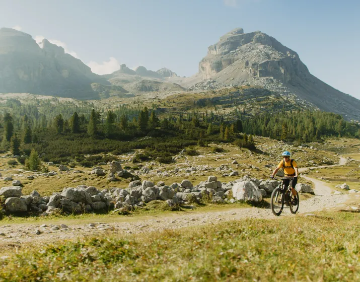 Ciclista di mountain bike su sentiero ghiaioso davanti a imponente scenario roccioso delle Dolomiti in estate presso Kronplatz