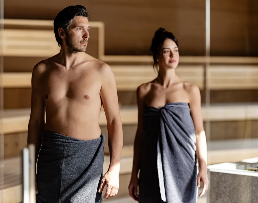 Paar in Handtüchern verlässt die Holzsauna im Wellnessbereich des Hotel Kronblick im Pustertal